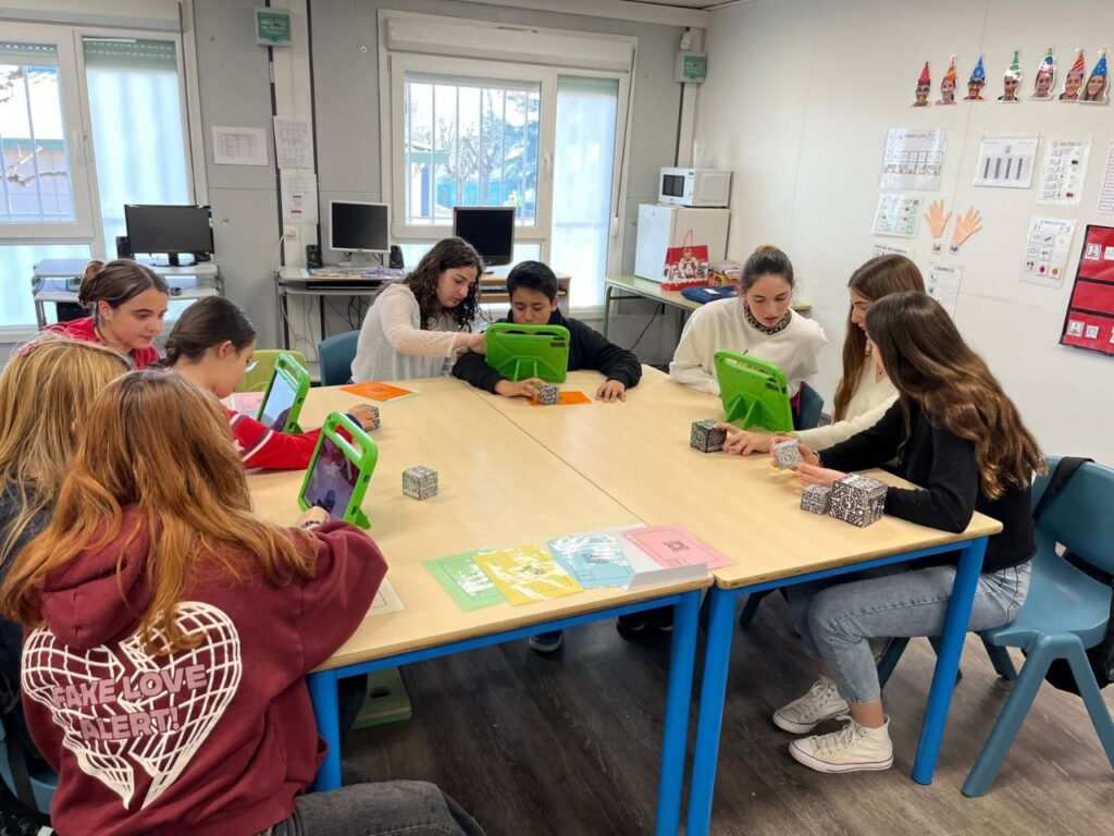 Nens asseguts al voltant d'una taula amb tablets enfocant differents cubs Merge
